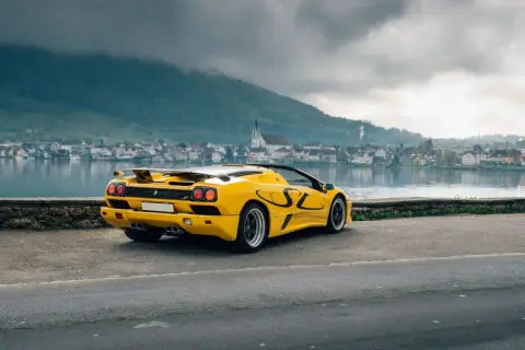 Żółty Lamborghini Diablo SV z czarnymi akcentami stoi nad jeziorem, w tle miasteczko i góry.