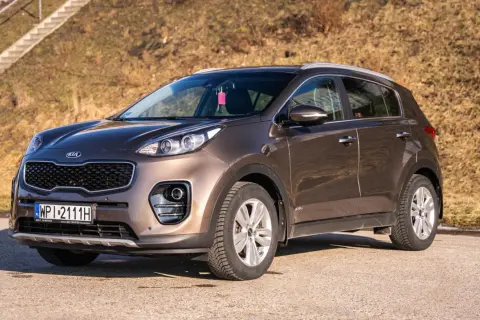 Brązowy Kia Sportage 2020 zaparkowany na tle suchej trawy i schodów.