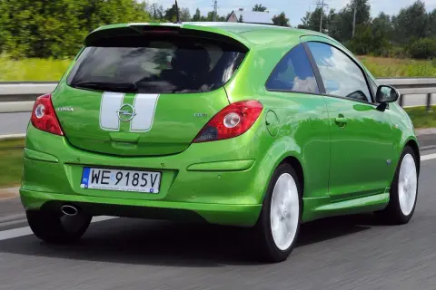 Zielony Opel Corsa D 1.2 benzyna z białymi pasami na klapie bagażnika jedzie po drodze.