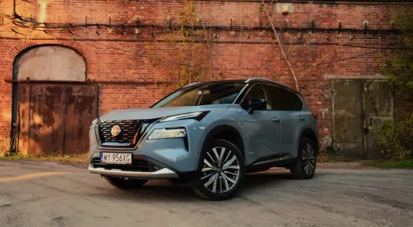 Szary Nissan X-Trail stoi przed starą ceglaną ścianą z zardzewiałymi drzwiami.