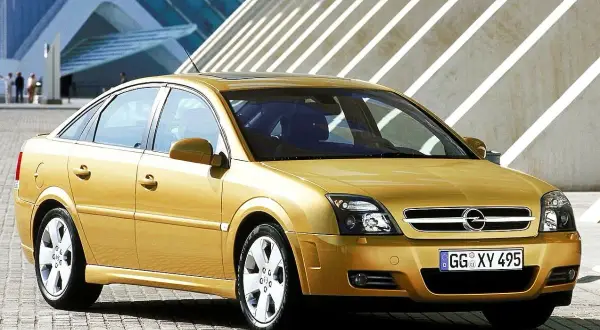 Złoty Opel Vectra C 1.9 CDTI 120 KM prezentuje się elegancko na tle nowoczesnej architektury. Opinie o tym modelu często podkreślają jego komfort i oszczędność.