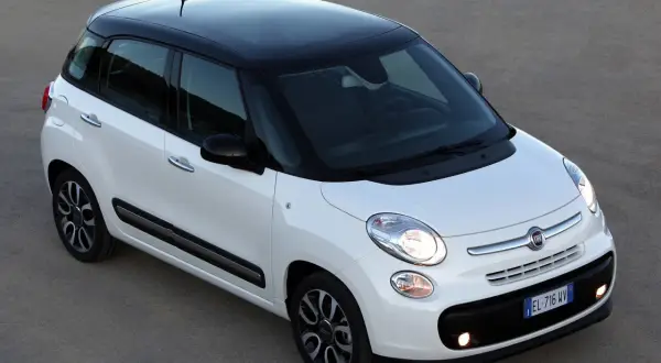 Biały Fiat 500L z czarnym dachem i felgami, zaparkowany na szarym podłożu.