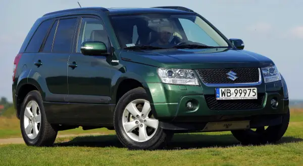 Zielony Suzuki Grand Vitara 2 na tle błękitnego nieba i zielonej trawy.
