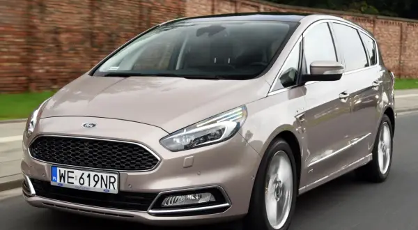 Beżowy Ford S-Max 2.0 TDCI w ruchu, z widocznym grillem i tablicą rejestracyjną WE 619NR.