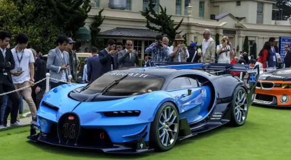 Niebieski Bugatti Chiron z numerem 16 na grillu, prezentowany na trawie, otoczony przez widzów robiących zdjęcia.