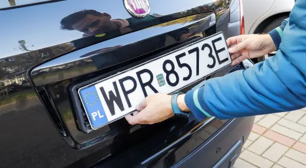 Ręce montują tablicę rejestracyjną WPR 8573E do czarnego Fiata. Zgubiona tablica rejestracyjna została odnaleziona.