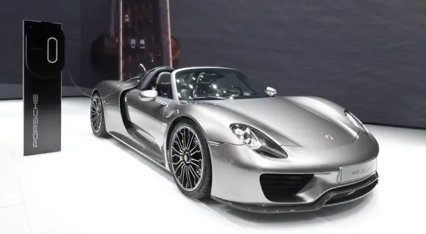 Srebrny Porsche 918 Spyder z zielonymi akcentami na felgach, gotowy do ładowania przy stacji Porsche.