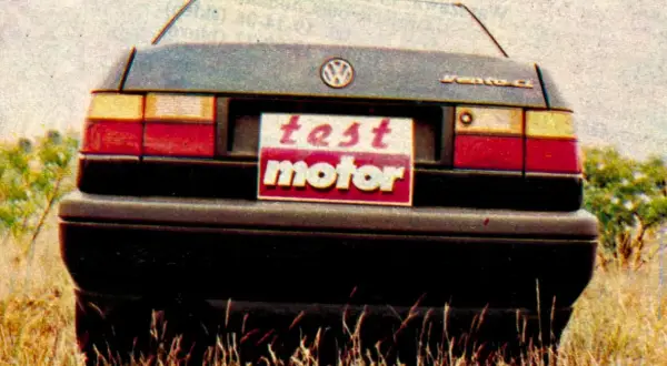 Tylna część Volkswagena Vento z tabliczką "test motor" na tle trawy i krzewów.