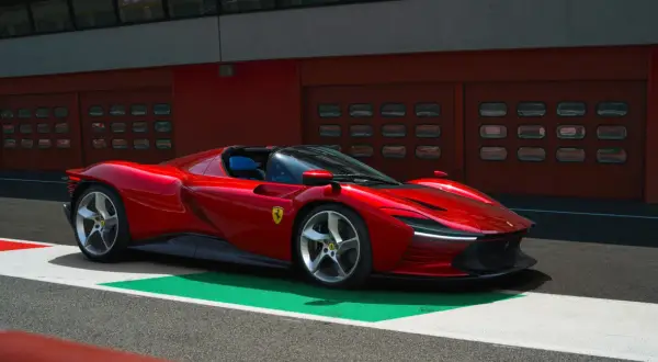 Czerwone Ferrari SP3 na torze wyścigowym, z niebieskimi siedzeniami i garażami w tle.