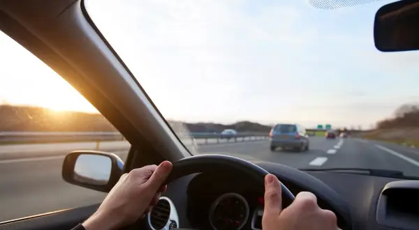 Ręce na kierownicy Toyoty Corolli, słońce zachodzi na autostradzie. Jak włączyć tempomat?