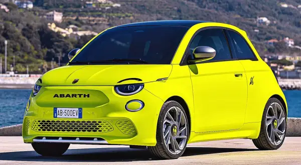 Jaskrawożółty Abarth 500 EV z czarnym dachem stoi na tle wzgórz i morza.