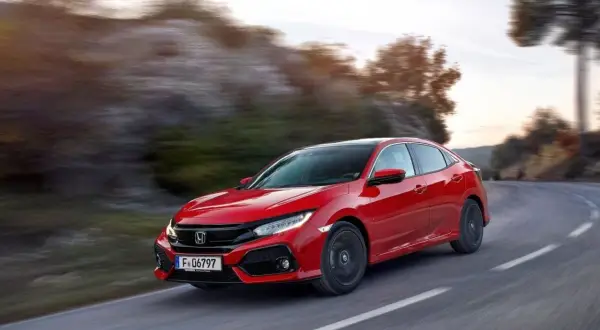 Czerwony Honda Civic 10 na zakręcie drogi, z rozmytym tłem gór i drzew.