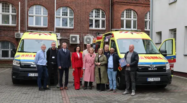 Grupa osób pozuje przed dwoma ambulansami. Jeden z mężczyzn trzyma dokument, być może związany z czn rejestracja.