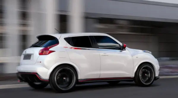 Biały Nissan Juke 1.5 dCi w wersji Nismo, z czerwonymi akcentami, pędzi ulicą. Jego sportowy wygląd budzi pozytywne opinie.