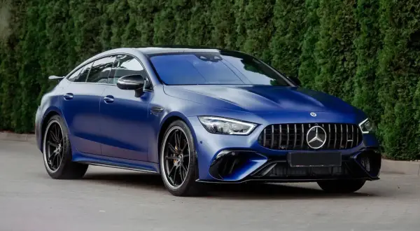 Niebieski matowy Mercedes-AMG GT 63 S z czarnymi felgami, zaparkowany przed żywopłotem.