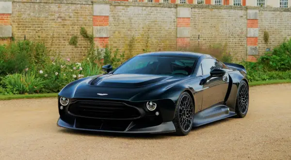 Elegancki, czarny Aston Martin Victor prezentuje się majestatycznie na tle zabytkowego dworu i bujnej zieleni.