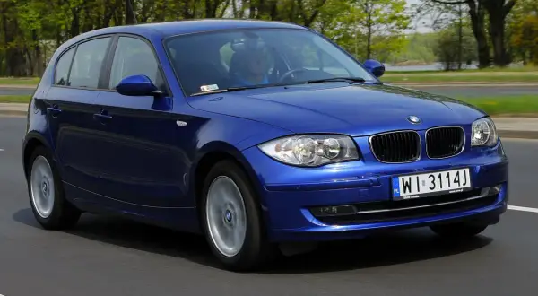 Niebieskie BMW E87 116i w ruchu, z widocznym kierowcą i tablicą rejestracyjną WI 3114J.