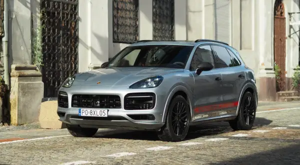 Srebrny Porsche Cayenne GTS z czerwonymi akcentami na progach, zaparkowany na brukowanej ulicy przed zabytkową kamienicą.