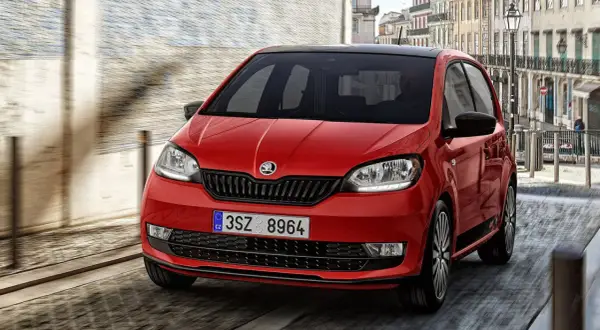 Czerwony Skoda Citigo z czarnym dachem pędzi ulicą miasta.