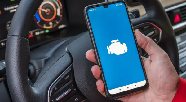 Ręka trzyma smartfon z ikoną silnika, gotowy do diagnostyki Toyoty. Jaki program do Toyoty z ELM327?