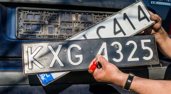 Ręce wymieniają tablice rejestracyjne. Jedna z nich, z numerem KXG 4325, jest przykręcana. To ważny etap w procesie rjs rejestracja.
