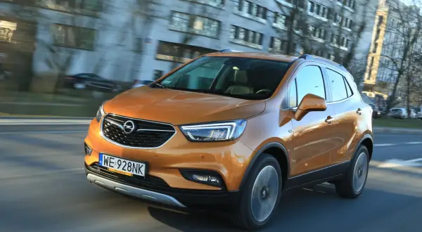 Pomarańczowy Opel Mokka 2015 pędzi ulicą, odbijając światła miasta w swojej lśniącej karoserii.