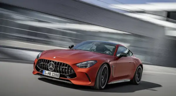 Pomarańczowy Mercedes-AMG GT 63 S pędzi obok nowoczesnej architektury.
