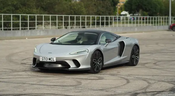 Srebrny McLaren GT z czarnym dachem, zaparkowany na placu z widocznymi śladami opon.