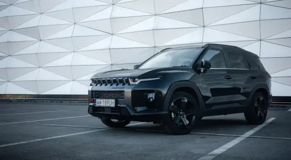 Czarny SsangYong Torres z czarnymi felgami stoi na parkingu przed nowoczesnym budynkiem o geometrycznej fasadzie.