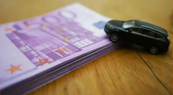 Czarny model samochodu na stosie banknotów 500 euro. Wartość rynkowa samochodu, tabela, urząd skarbowy - wszystko w jednym kadrze.
