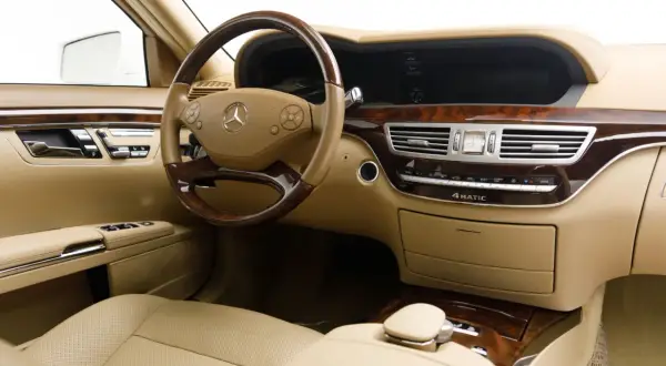 Wnętrze luksusowego Mercedesa S 500 z beżową skórzaną tapicerką, drewnianymi wstawkami i kierownicą.