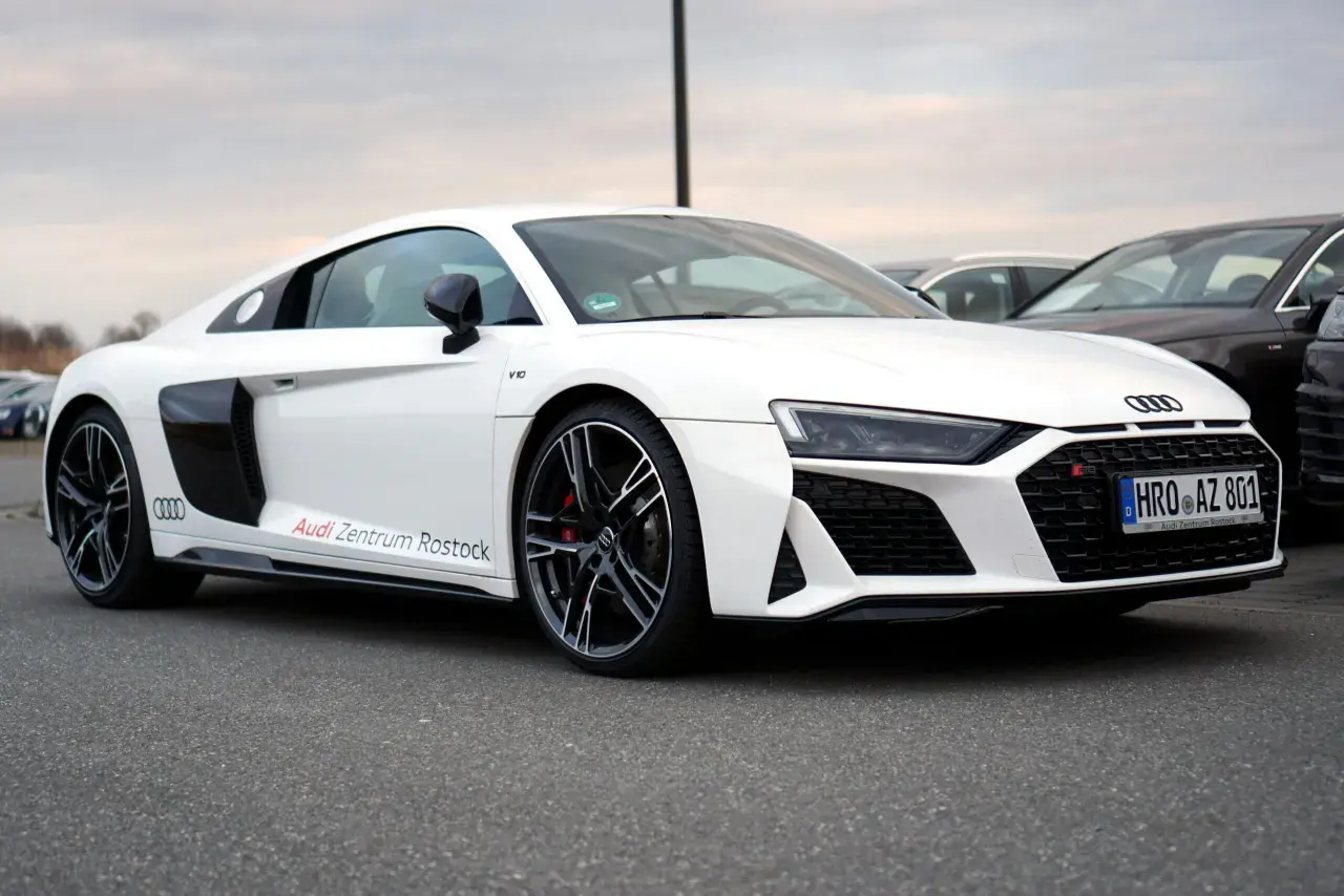 Białe Audi R8 V10 z napisem "Audi Zentrum Rostock" na progu, zaparkowane na zewnątrz.