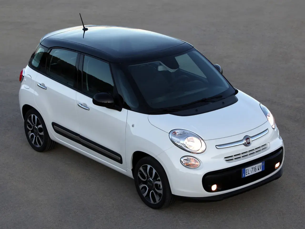 Biały Fiat 500L z czarnym dachem i felgami, zaparkowany na szarym podłożu.
