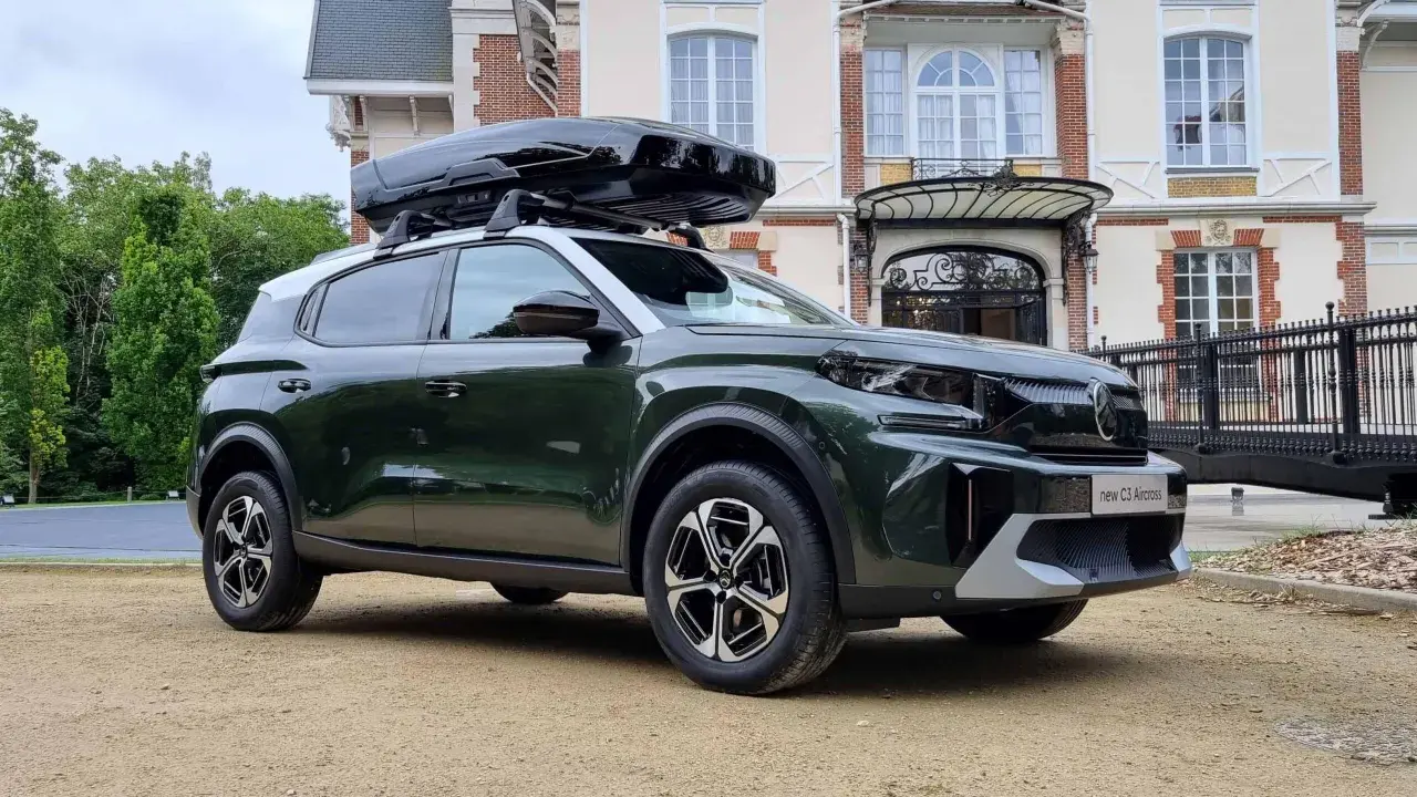 Nowy C3 Aircross w ciemnozielonym kolorze z czarnym boxem dachowym przed eleganckim budynkiem.