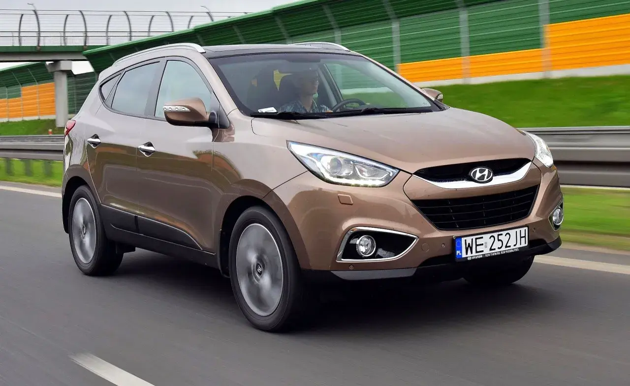 Brązowy Hyundai i35 na drodze, z zielono-żółtymi barierami dźwiękochłonnymi w tle.