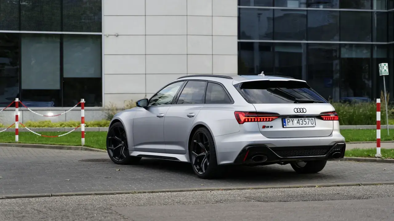 Srebrne Audi RS6 Avant z czarnymi felgami stoi na parkingu przed nowoczesnym budynkiem.
