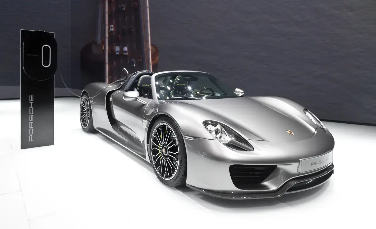Srebrny Porsche 918 Spyder z zielonymi akcentami na felgach, gotowy do ładowania przy stacji Porsche.