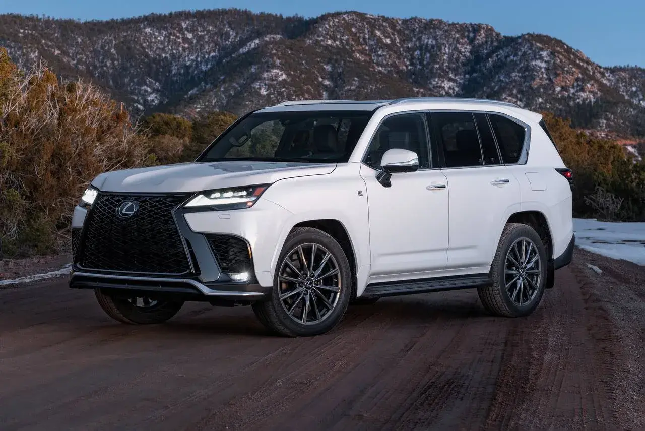 Biały Lexus LX 600 na drodze gruntowej, z ośnieżonymi górami w tle.