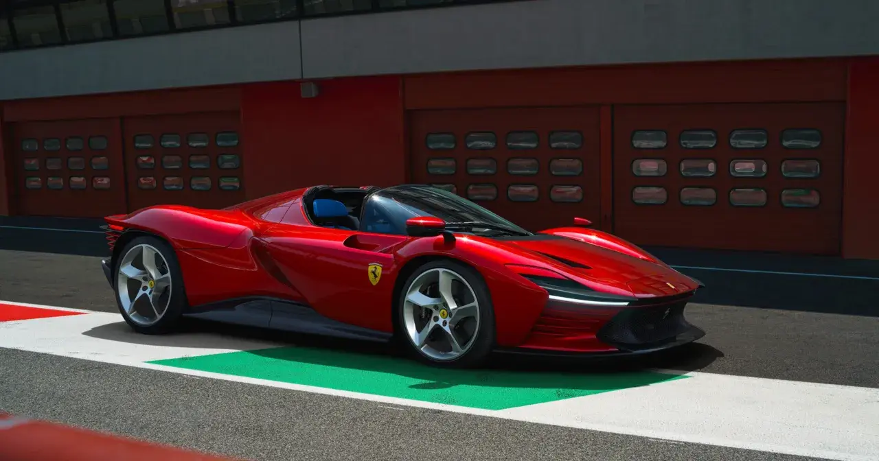 Czerwone Ferrari SP3 na torze wyścigowym, z niebieskimi siedzeniami i garażami w tle.