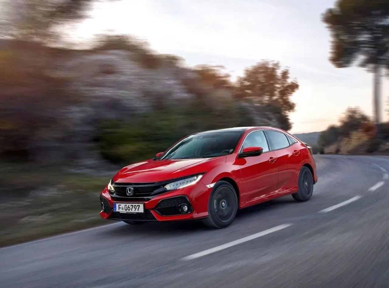 Czerwony Honda Civic 10 na zakręcie drogi, z rozmytym tłem gór i drzew.