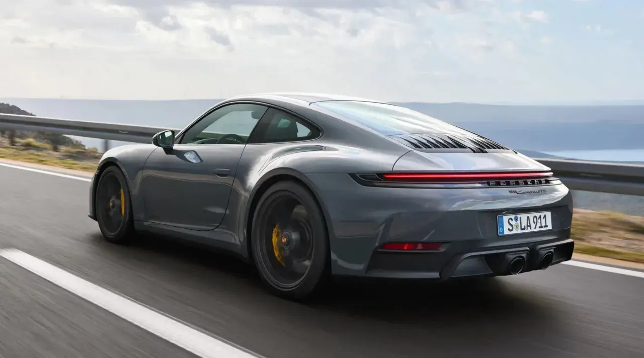 Szary Porsche 911 GTS pędzi po krętej drodze z widokiem na morze.