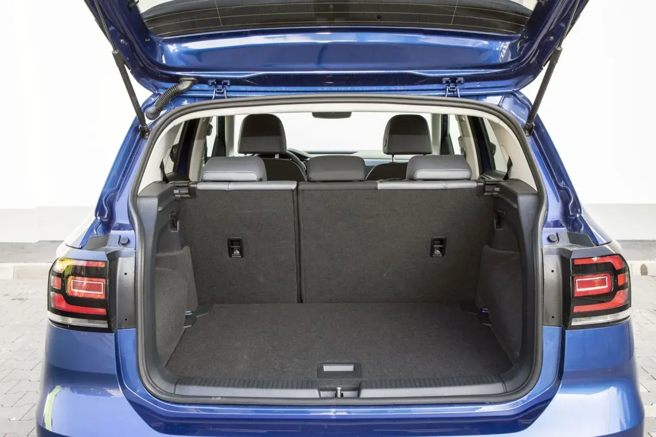 Błękitny Volkswagen T-Cross z otwartym bagażnikiem. Widać tylne siedzenia i przestronną przestrzeń bagażową, idealną na wakacyjne wyjazdy.