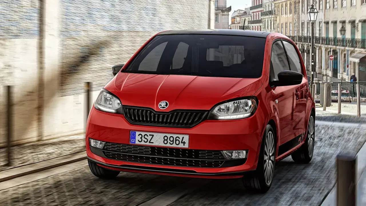 Czerwony Skoda Citigo z czarnym dachem pędzi ulicą miasta.