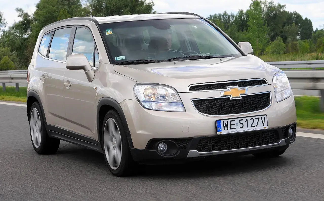 Złoty Chevrolet Orlando na drodze. Kierowca w środku. Wiele osób szuka chevrolet orlando opinie, ten samochód może być dobrym wyborem.