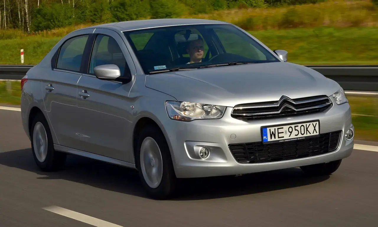 Srebrny Citroen C Elysee jedzie po drodze, za kierownicą siedzi mężczyzna.