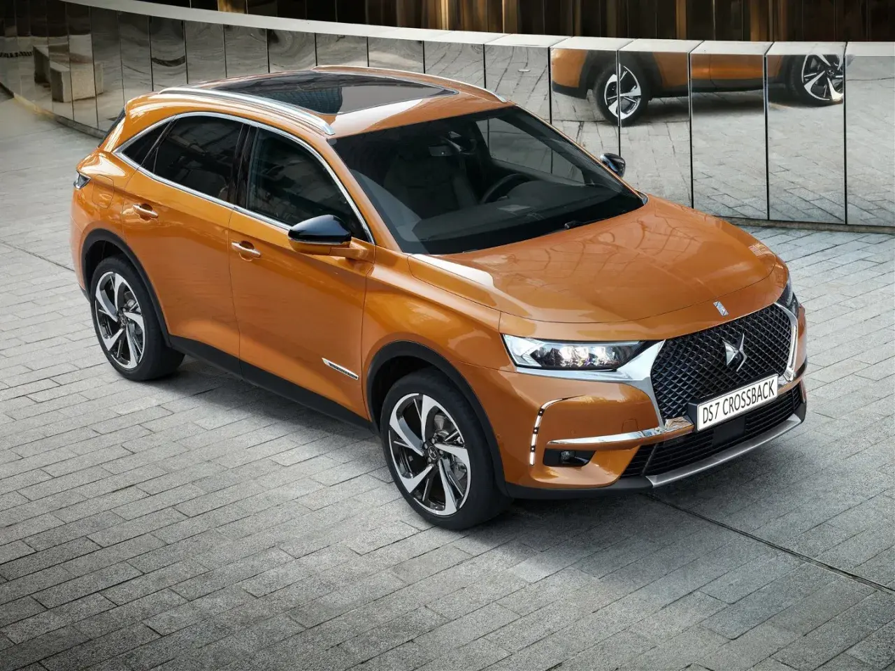 Pomarańczowy Citroën DS7 Crossback lśni na tle lustrzanej ściany. Elegancki SUV prezentuje swoje nowoczesne linie.