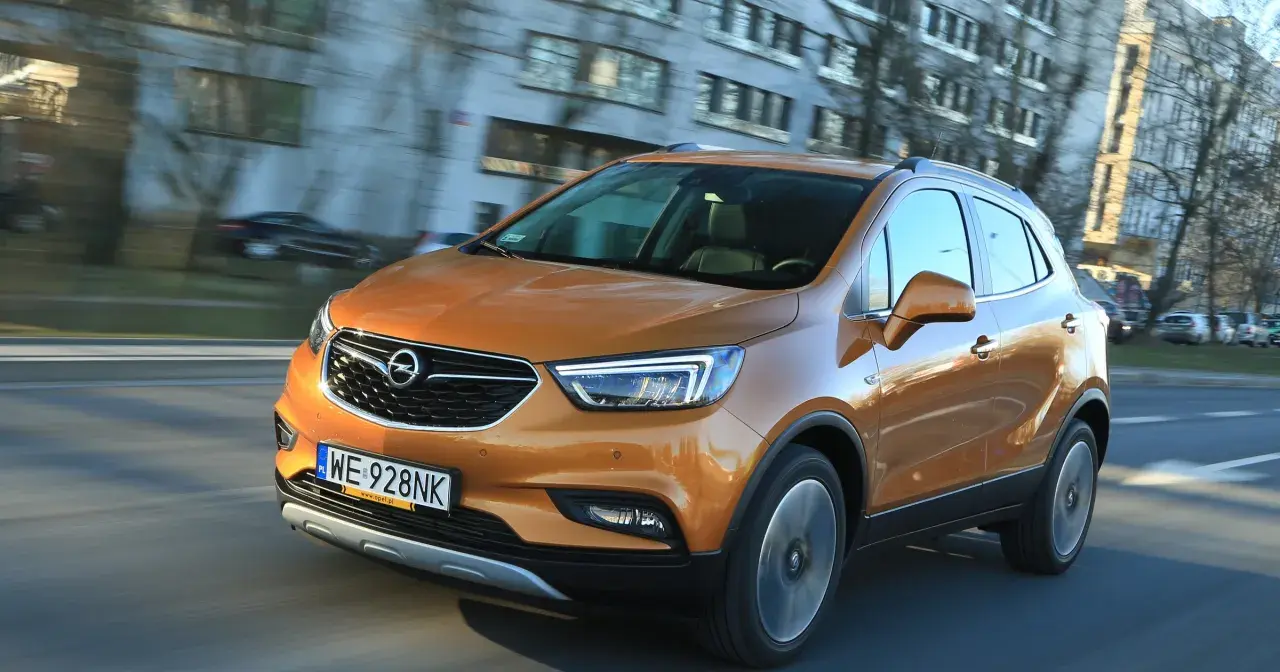 Pomarańczowy Opel Mokka 2015 pędzi ulicą, odbijając światła miasta w swojej lśniącej karoserii.