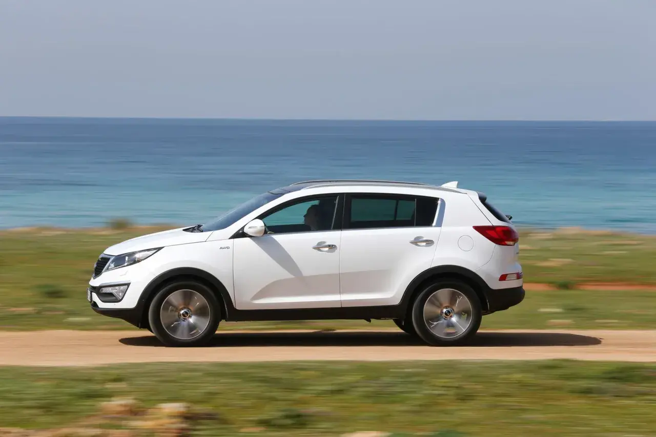 Biały Kia Sportage 2013 jedzie przy błękitnym morzu.