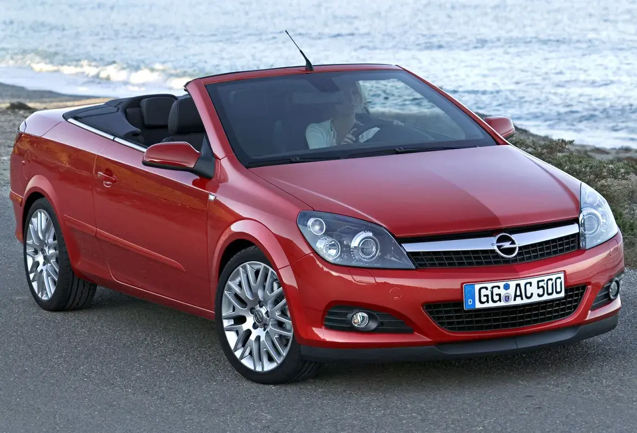 Czerwony opel cabrio z opuszczonym dachem, zaparkowany przy plaży. Kobieta za kierownicą cieszy się jazdą.