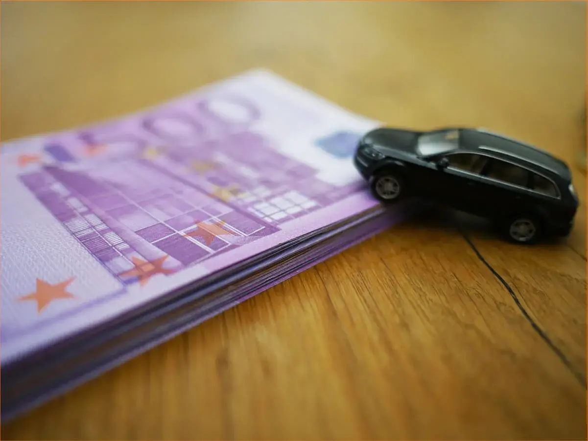 Czarny model samochodu na stosie banknotów 500 euro. Wartość rynkowa samochodu, tabela, urząd skarbowy - wszystko w jednym kadrze.